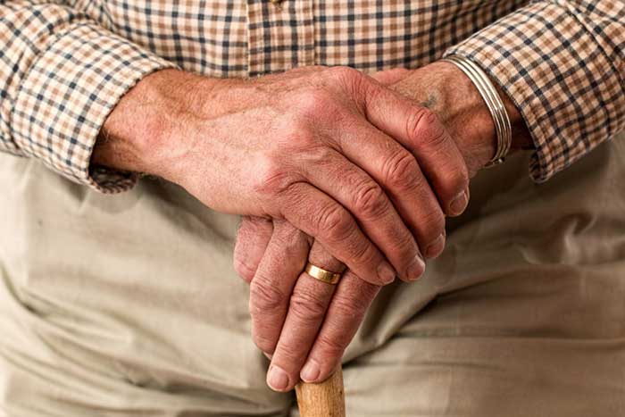 A Canadian senior who is in debt holding his hands together on his cane